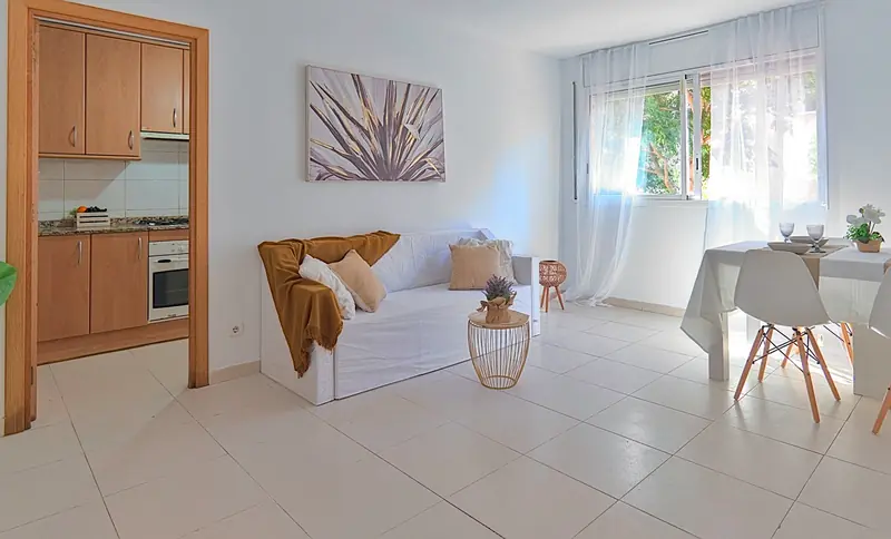 Salón luminoso con sofá blanco, comedor y cocina independiente