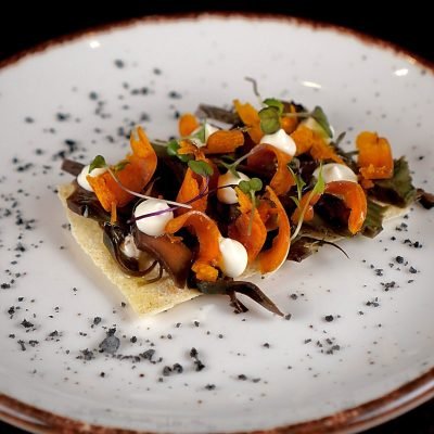 Plato gourmet con base crujiente, vegetales naranjas, brotes verdes y salsa, fotografía gastronómica en Barcelona por Click Lab.