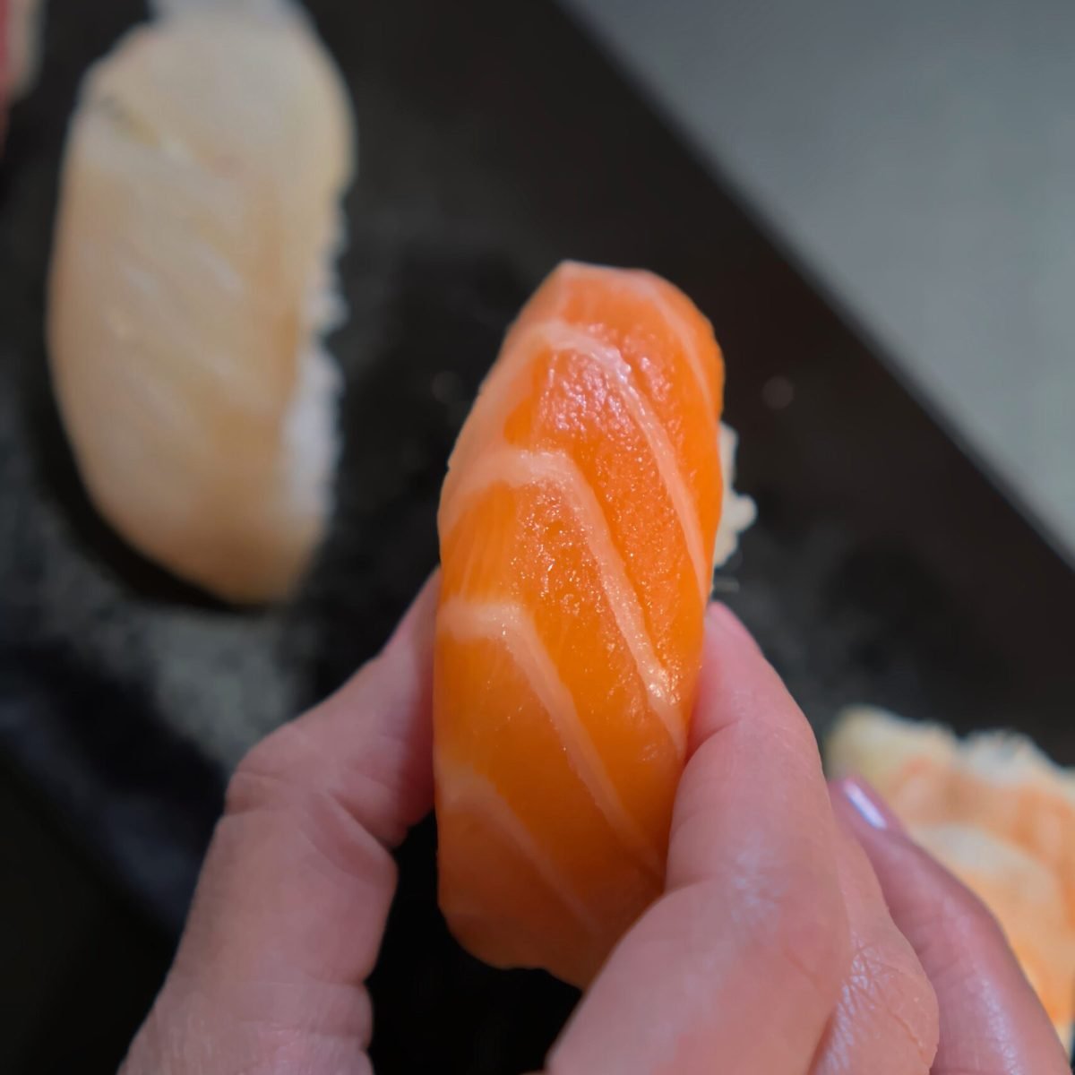 Mano sosteniendo un nigiri de salmón fresco, fotografía gastronómica profesional para restaurantes japoneses en Barcelona.