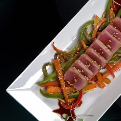 Plato rectangular con lomos de atún rojo sellado, verduras salteadas y sésamo, fotografía gastronómica profesional en Barcelona.