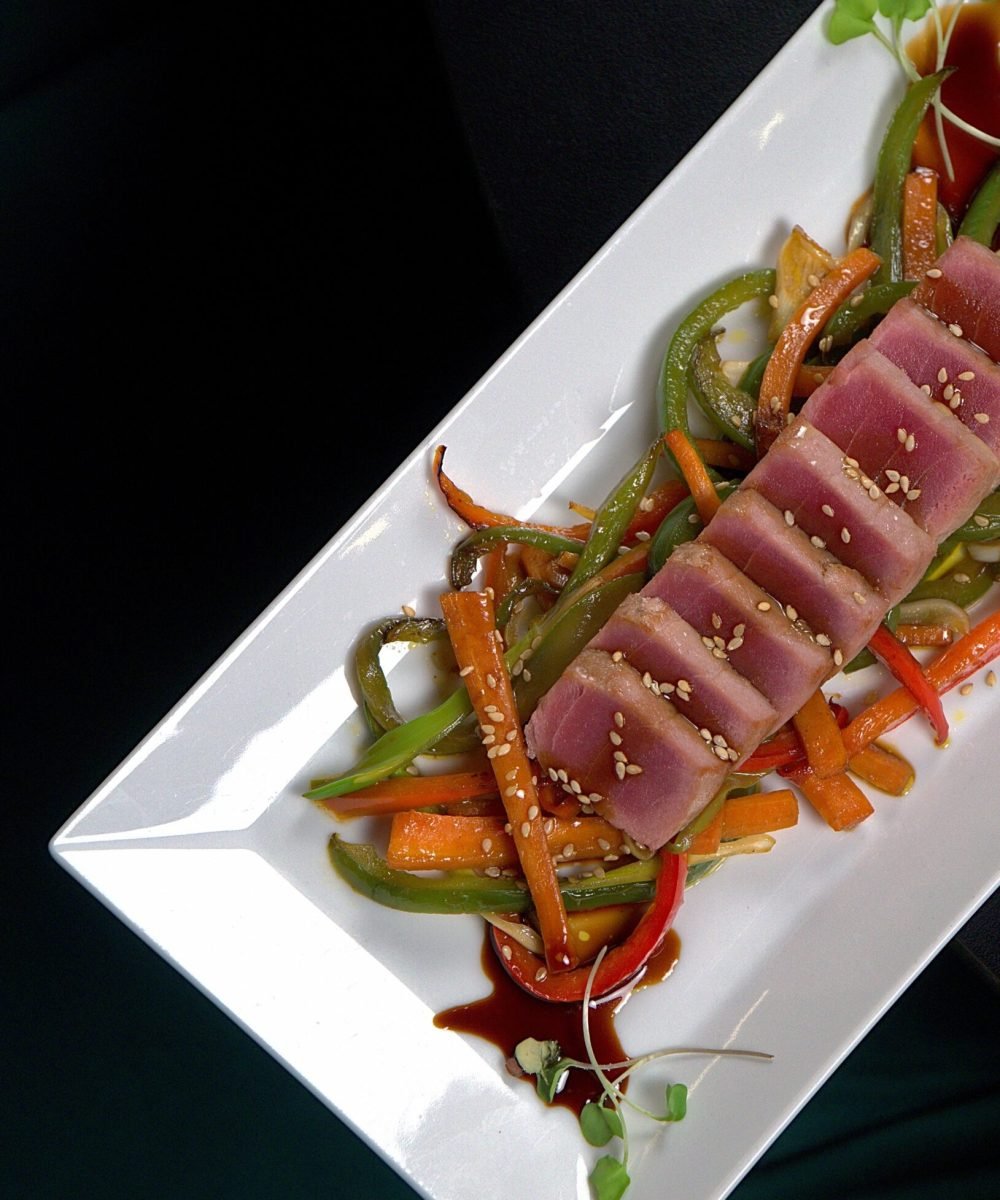 Plato rectangular con lomos de atún rojo sellado, verduras salteadas y sésamo, fotografía gastronómica profesional en Barcelona.